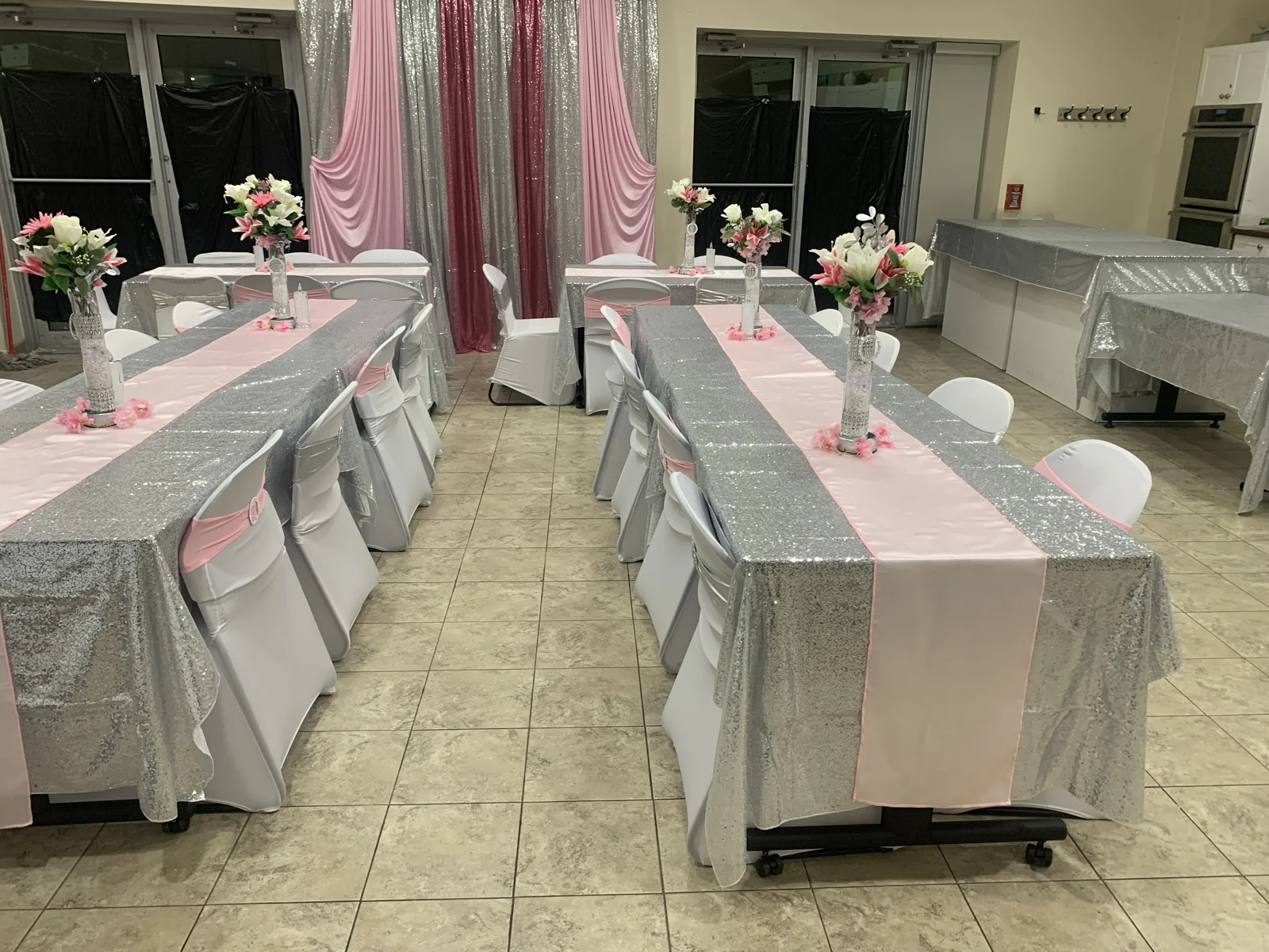 Full-room view of pink runners, silver linens, floral centrepieces and a pink-and-silver draped backdrop